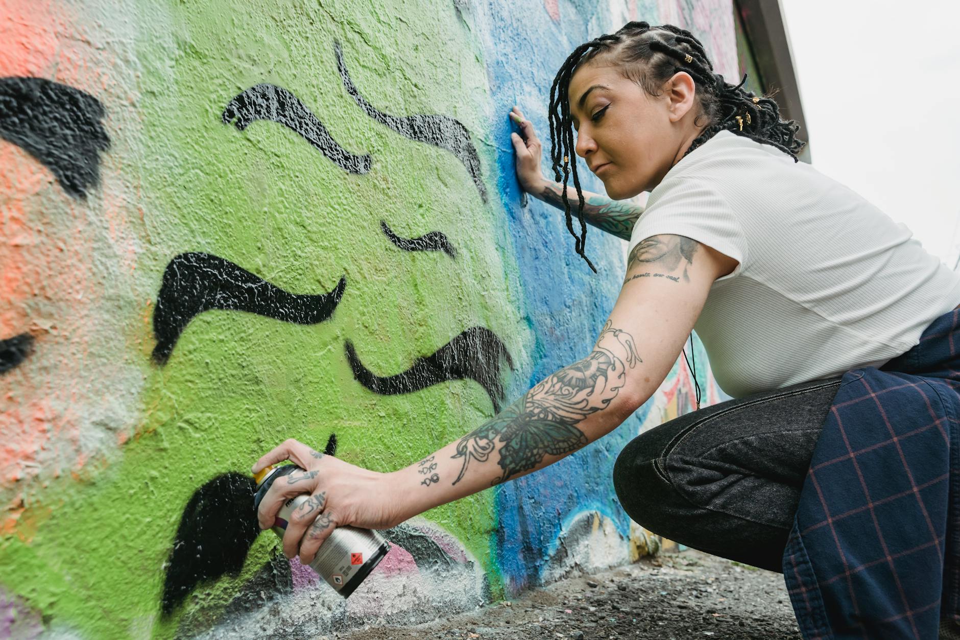 Kobieta maluje kolorowe graffiti sprayem na ścianie w mieście