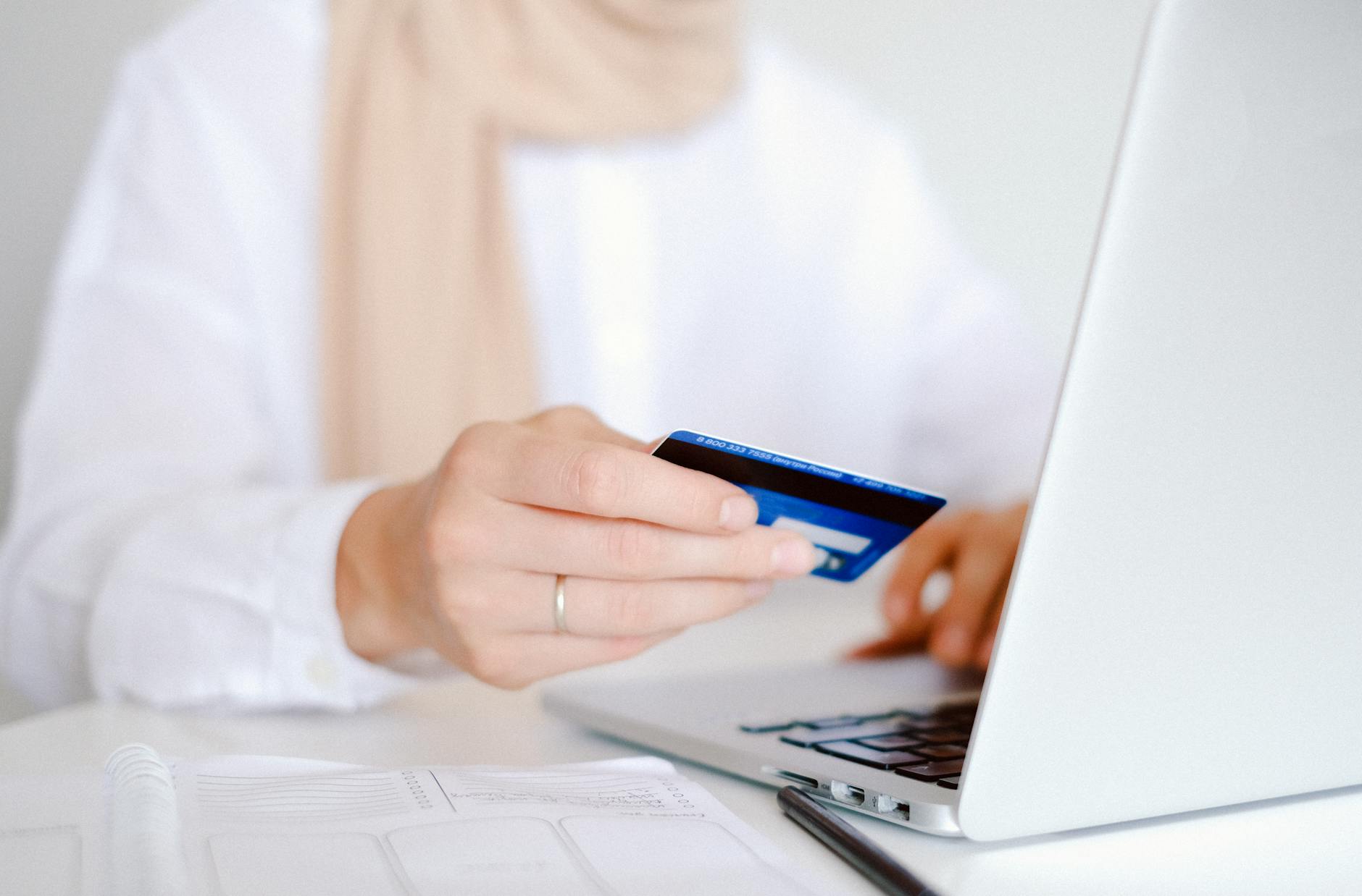 Osoba trzyma kartę płatniczą przy laptopie podczas zakupów online