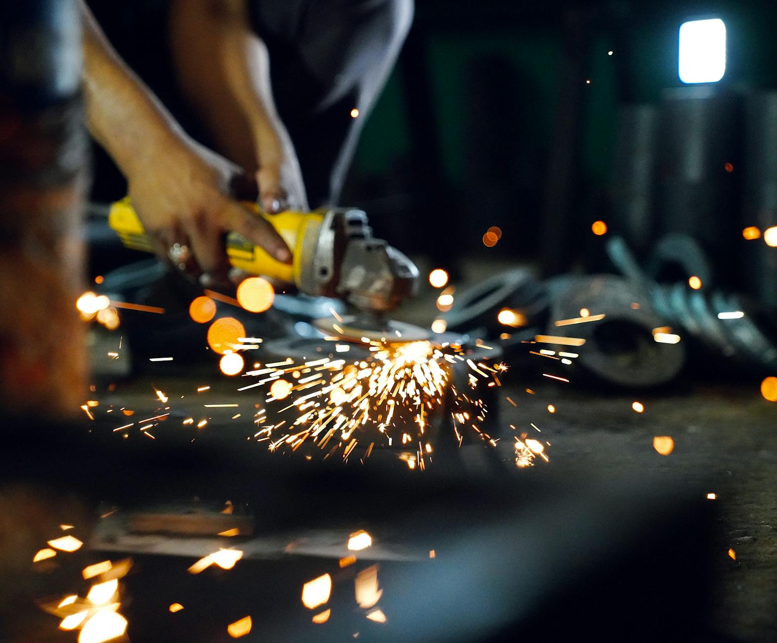 Pracownik szlifuje metal szlifierką kątową, z której sypią się iskry