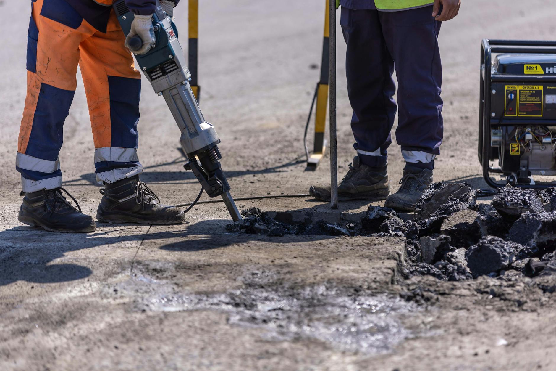 Robotnicy z młotem pneumatycznym rozbijają asfalt na drodze