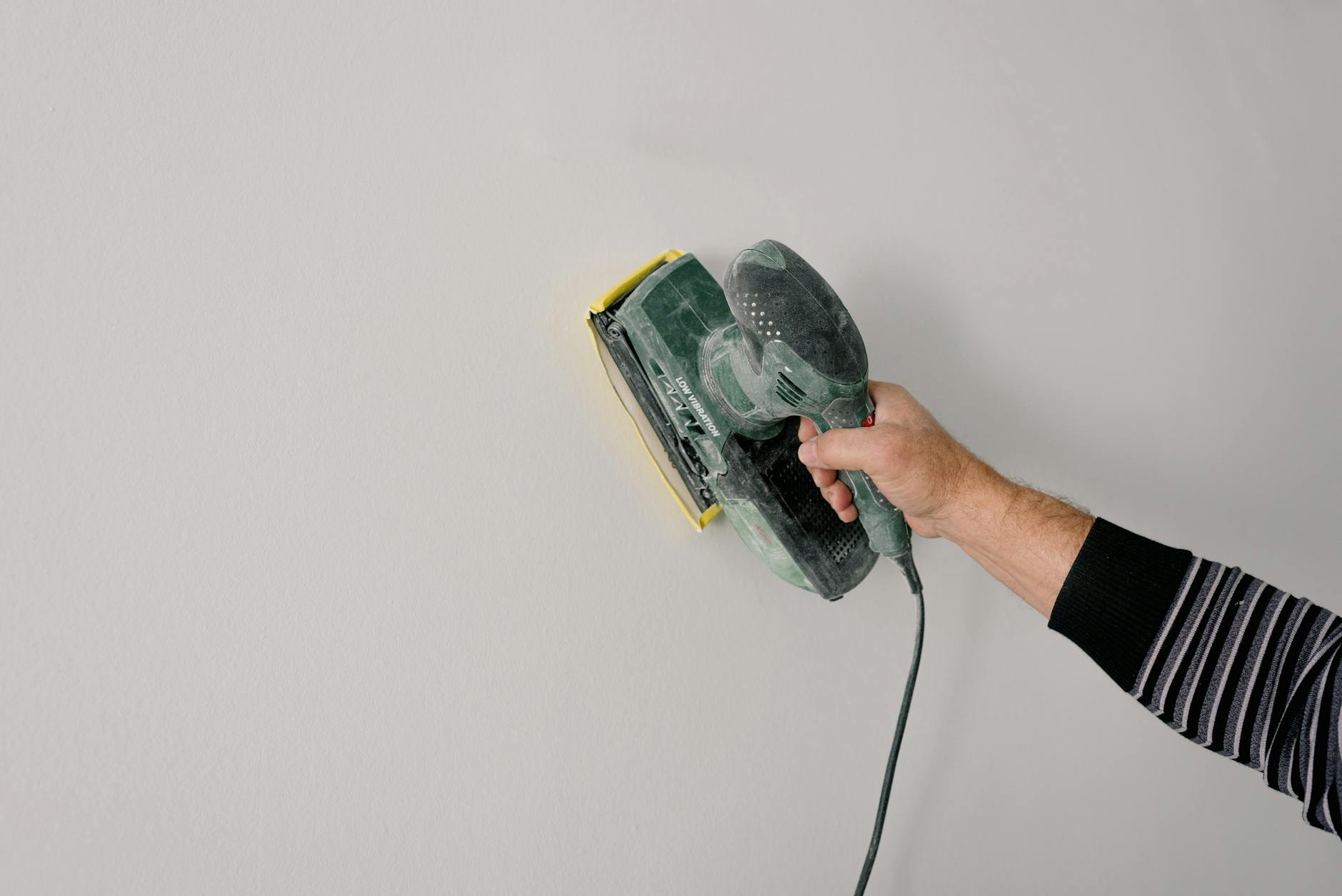 Szlifowanie gładzi ściennej elektryczną szlifierką podczas remontu