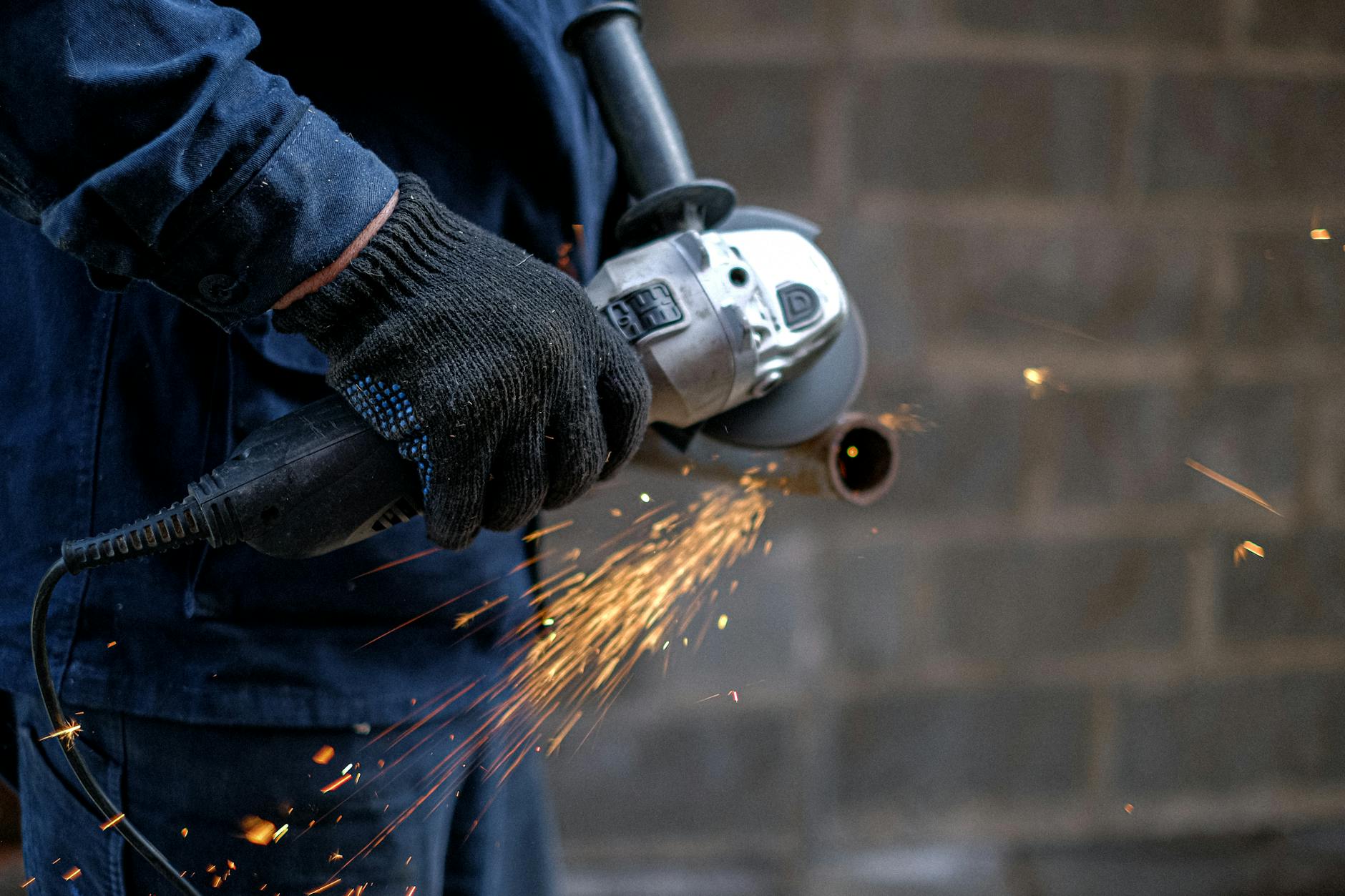 Pracownik tnie metal szlifierką kątową, z tarczy sypią się iskry