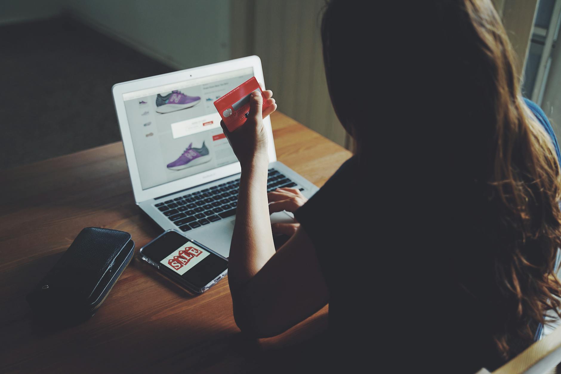 Kobieta kupuje online przy biurku, trzymając kartę płatniczą