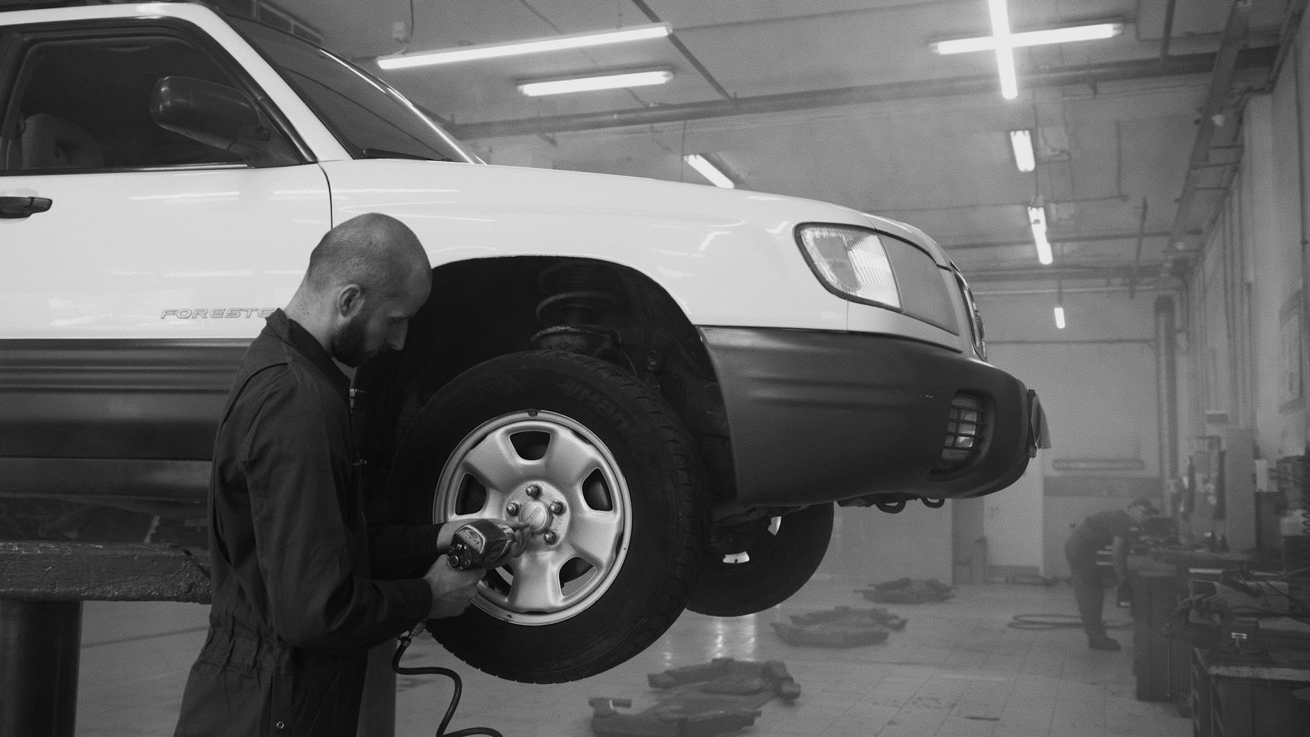 Mechanik dokręca koło samochodu kluczem udarowym w warsztacie