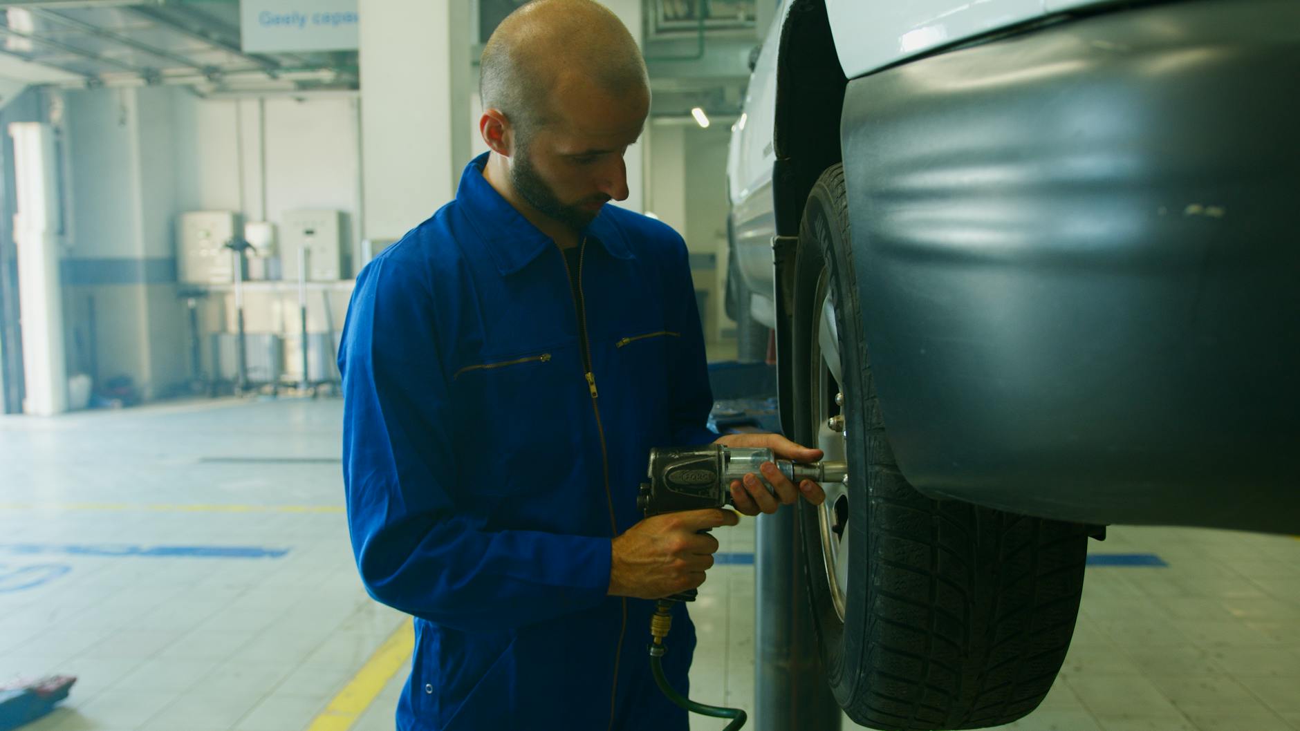 Mechanik w niebieskim kombinezonie odkręca koło kluczem udarowym w warsztacie
