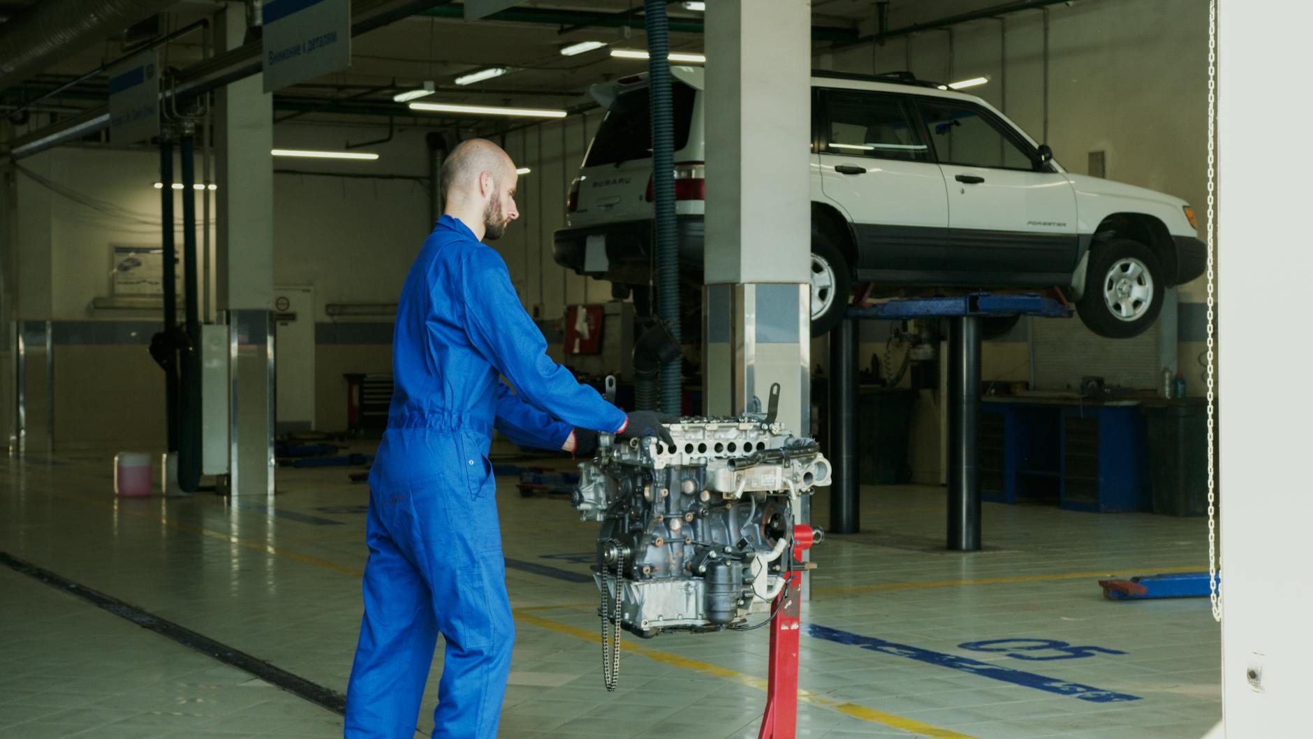 Mechanik w niebieskim kombinezonie serwisuje silnik w warsztacie samochodowym