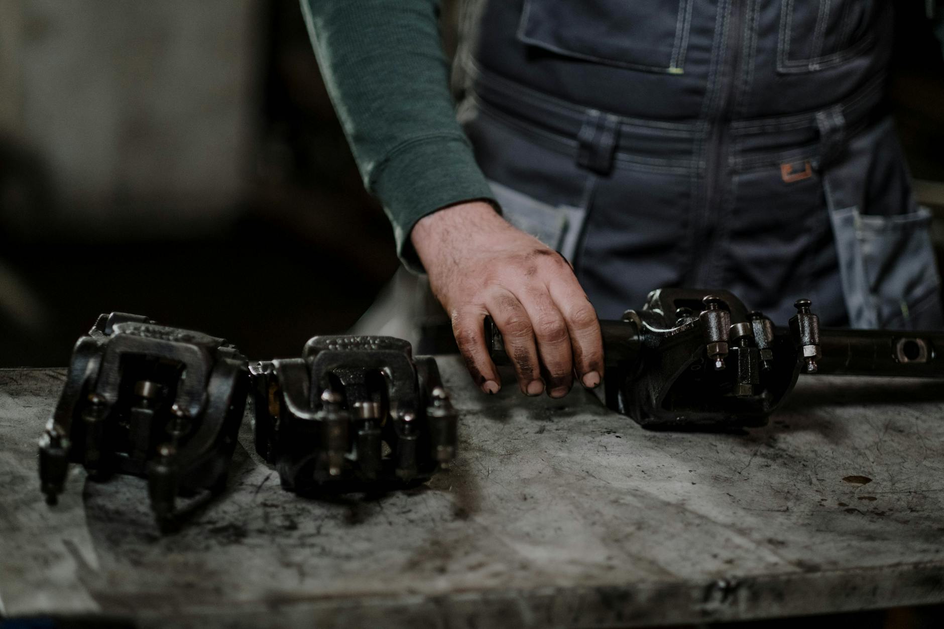 Mechanik w warsztacie trzyma zabrudzone smarem metalowe części na stole