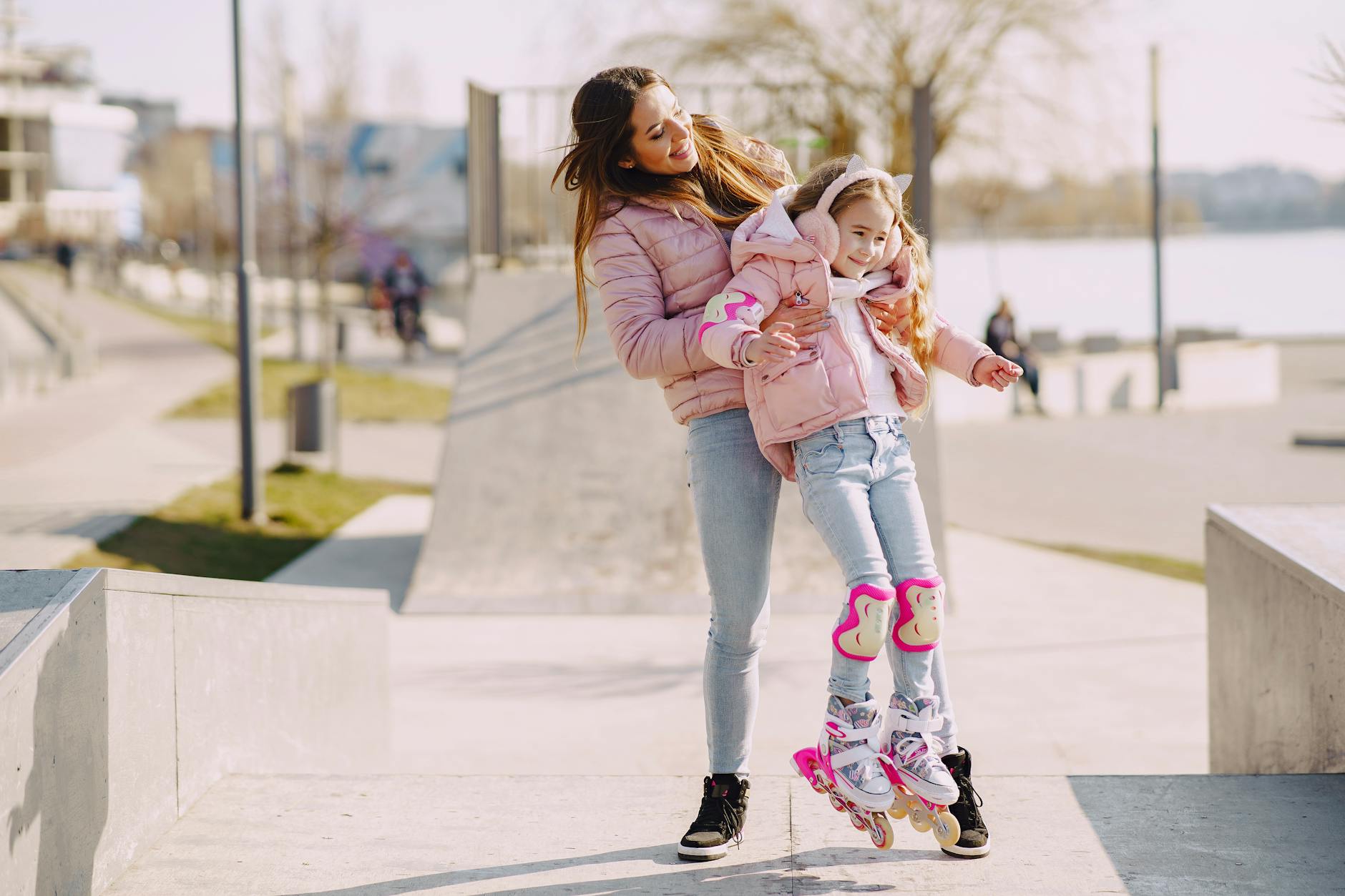 Mama uczy córkę jazdy na rolkach w kasku i ochraniaczach na skateparku