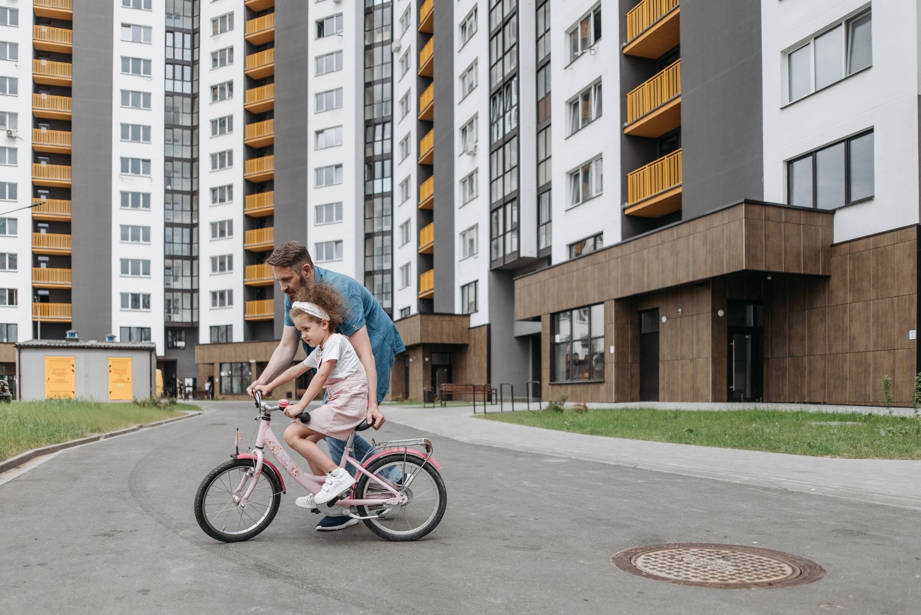 Ojciec uczy córkę jeździć na rowerze przed nowoczesnymi blokami