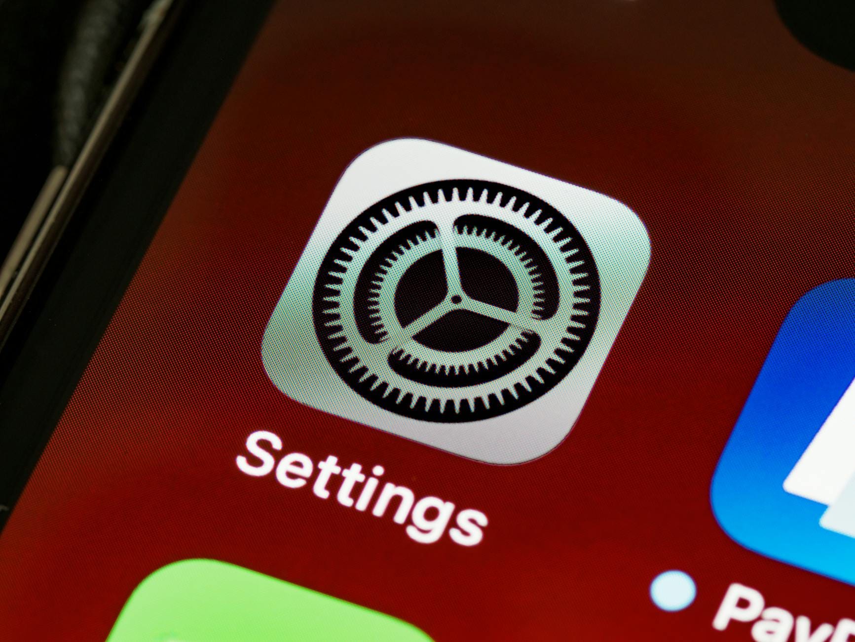 Zbliżenie ekranu iPhone’a z ikoną ustawień na tle ciemnego interfejsu Zbliżenie ekranu iPhone’a z ikoną ustawień na tle ciemnego interfejsu
