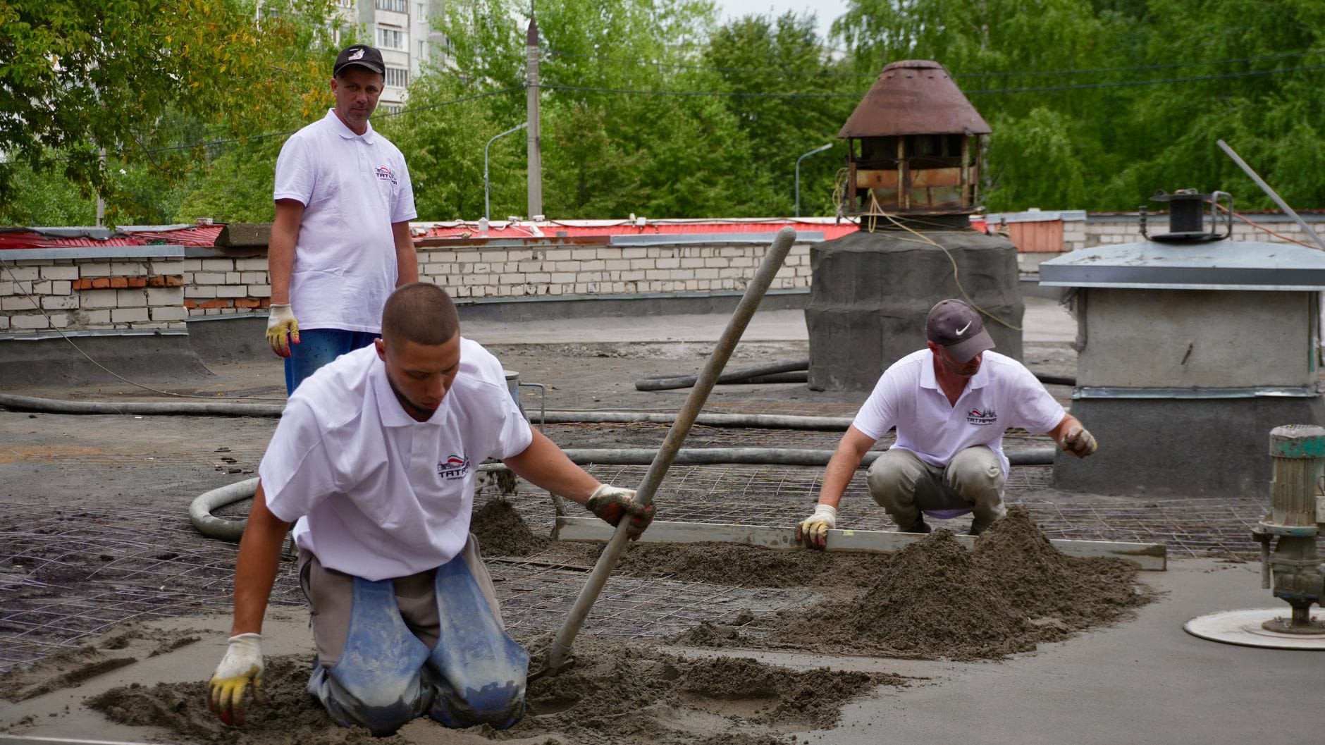 Trzej pracownicy zacierają i wyrównują beton na dachu budowy